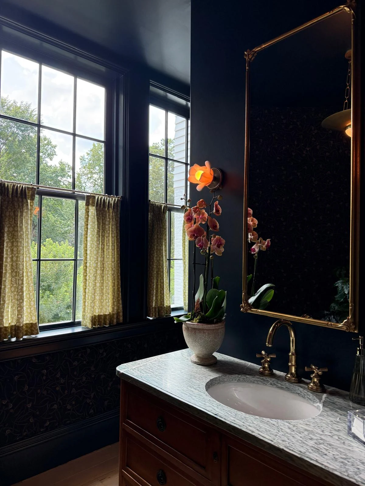 Honed marble vanity with unlacquered brass fixtures and botanical lighting